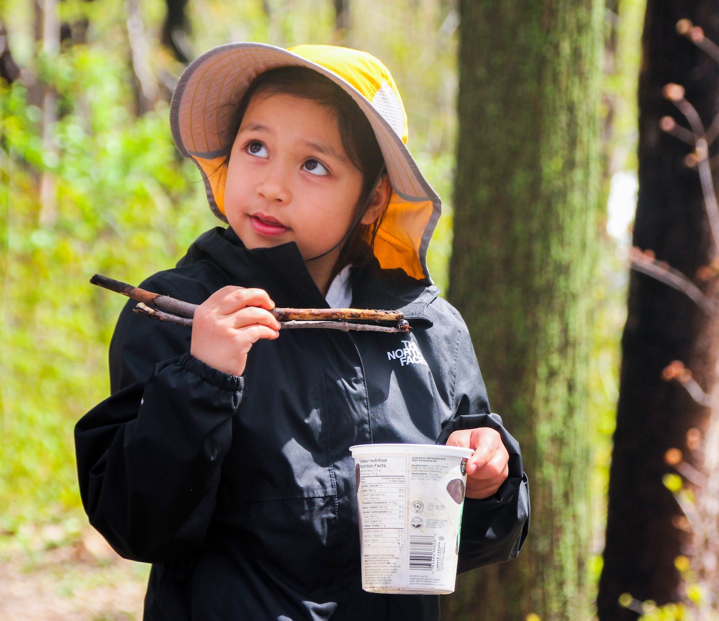 a child in the forest holding a stick and a container