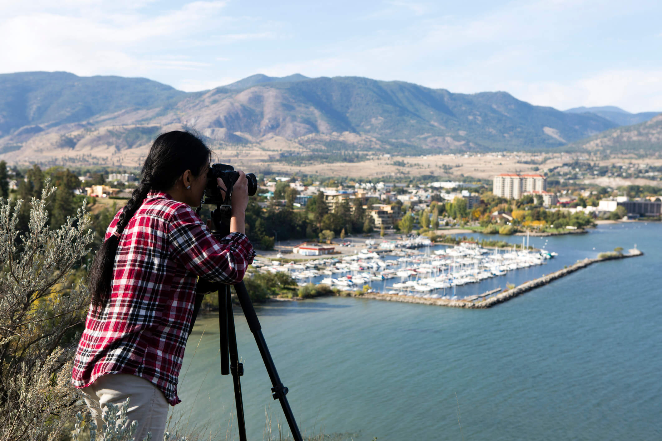 Person takes photo overlooking water and city, with mountains in the background